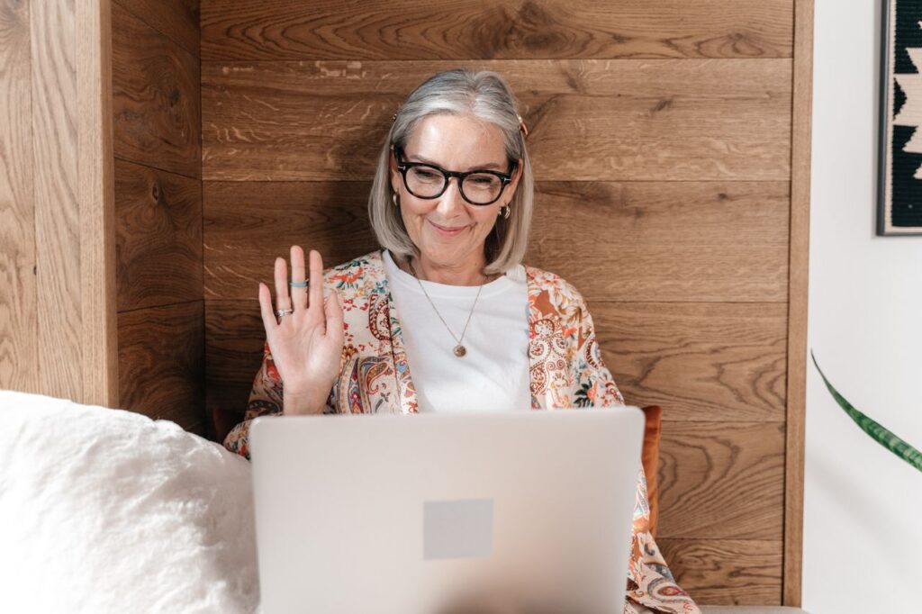 Elderly woman using a laptop for a video call, relaxing indoors.